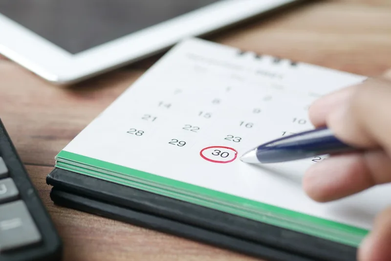 A person writing on a desk calendar, planning a consistent weekly content upload schedule