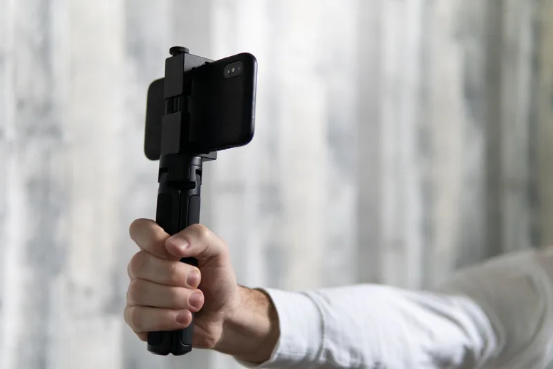 Close-up of a person holding a smartphone attached to a tripod for stability